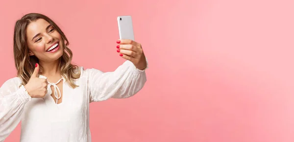 Крупный план портрет стильной красивой красоты блоггер записывает видео на смартфон, делает селфи, показывает большие пальцы вверх на камеру мобильного телефона, улыбаясь приятно, рекомендую место для последователей — стоковое фото