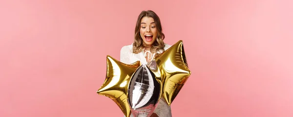 Holidays, celebration and women concept. Portrait of happy lovely young woman in white dress, gasping from amazement and joy, holding birthday star-shaped balloons, pink background — Stock Photo, Image