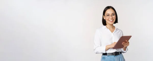 하얀 배경 위에 서서 웃으며 디지털 태블릿을 들고 있는 안경을 쓴 젊은 이시아 여성의 사진 — 스톡 사진