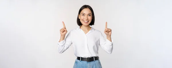 Femme d'affaires asiatique enthousiaste pointant, regardant vers le haut avec un visage souriant heureux, montrant le logo ou la bannière de l'entreprise, debout sur fond blanc — Photo