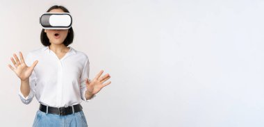 Sanal gerçeklikteki hayret verici genç kadın, VR gözlük takıyor, beyaz arka planda duruyor.