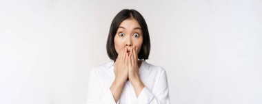 Suratı asyalı bir kadının soluk soluğa kalmış, şok olmuş ve nutku tutulmuş bir halde el ele tutuşmuş, kameraya bakıyor, etkilenmiş, beyaz arka plan