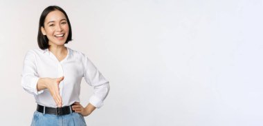 Kendine güvenen Asyalı bir kadının gülümsemesi, el sıkışma hareketi için elini uzatması, merhaba demesi, beyaz arka planda durması.