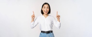 Hevesli Asyalı iş kadını, mutlu bir gülümsemeyle yukarı bakıyor, şirket logosunu ya da afişini gösteriyor, beyaz arka planda duruyor.
