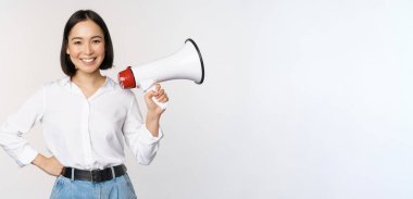 Gülümseyen genç Asyalı kadın megafonla poz veriyor, haber konsepti, duyuru ve bilgi, beyaz arka planda duruyor.