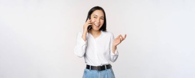 Dost canlısı gülümseyen Asyalı kadın telefonda konuşuyor, nöbetçi kız, akıllı telefonu tutuyor ve gülüyor, konuşuyor, beyaz arka planda duruyor.