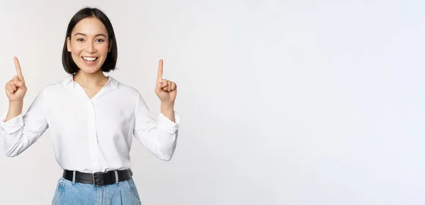 Bild einer lächelnden selbstbewussten Geschäftsfrau, asiatische Dame, die mit dem Finger nach oben zeigt, Banner oder Verkaufsinformationen zeigt, vor weißem Hintergrund stehend — Stockfoto