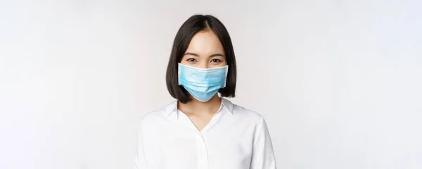 Covid och sjukvård koncept. Närbild porträtt av asiatisk kvinna, kontor dam i ansiktsmask, leende, med skydd mot coronavirus under pandemi, vit bakgrund — Stockfoto