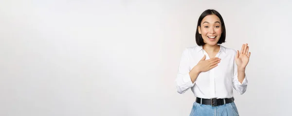 Bild der netten jungen Büroangestellten, asiatischen Studentin hebt die Hand nach oben und legt die Handfläche auf die Brust, benennt sich, stellt sich vor, macht Versprechen, steht über weißem Hintergrund — Stockfoto