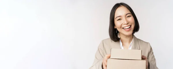 Bild der asiatischen Verkäuferin, Geschäftsfrau, die Kisten mit Bestellung gibt, Kunden ausliefert, im Anzug vor weißem Hintergrund steht — Stockfoto