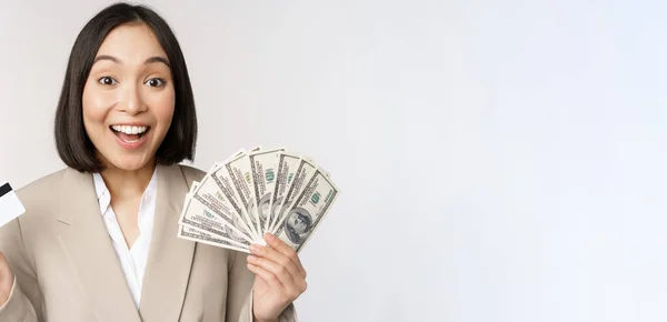 Wanita pengusaha muda Asia yang antusias, menunjukkan uang dan kartu kredit, berdiri di atas latar belakang putih — Stok Foto