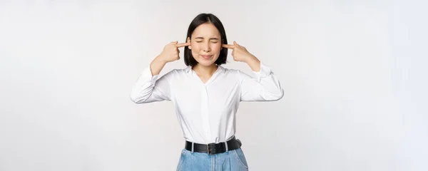 Ενοχλημένη Ασιάτισσα που νιώθει δυσφορία από δυνατό ενοχλητικό θόρυβο, κοντά αυτιά και μάτια, στέκεται πάνω από λευκό φόντο — Φωτογραφία Αρχείου