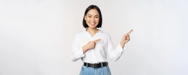 Retrato de hermosa mujer asiática, vendedora señalando los dedos a la derecha y mostrando información, pancarta o logotipo, publicidad de venta, de pie sobre fondo blanco —  Fotos de Stock