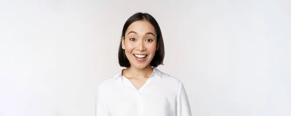 Close up retrato de jovem asiático modelo feminino olhando espantado para a câmera, sorrindo dentes brancos, de pé contra fundo branco — Fotografia de Stock