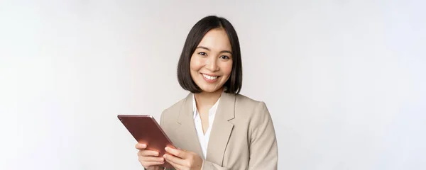 Immagine di donna d'affari asiatica, commessa con tablet digitale e sorridente, che lavora con gadget, in piedi in abito su sfondo bianco — Foto Stock