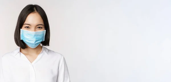 Concepto de covidio y salud. Primer plano retrato de mujer asiática, señora de la oficina en la máscara de la cara, sonriendo, utilizando la protección contra el coronavirus durante la pandemia, fondo blanco —  Fotos de Stock
