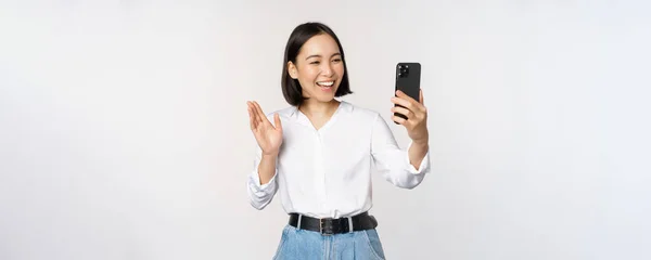 세련 된 현대의 동양 여성 이 스마트폰 전면 카메라로 손을 흔드는 모습, 비디오 채팅, 휴대 전화 앱으로 사람 과 채팅하는 모습, 흰색 배경 — 스톡 사진