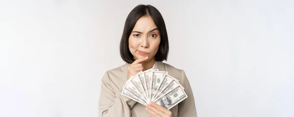 Citra wanita perusahaan Asia, pengusaha bahagia yang menunjukkan uang, dolar tunai dan berpikir, berdiri di atas latar belakang putih — Stok Foto