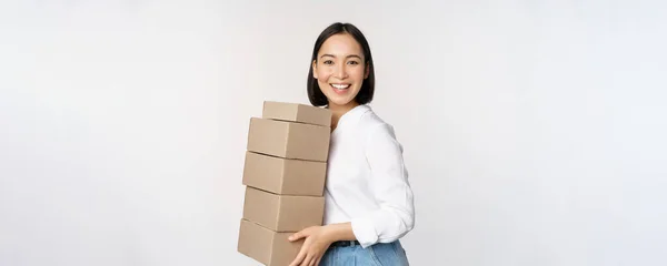 Imagen de mujer asiática sonriente, feliz sosteniendo pila de cajas, concepto de entrega, compras o negocios, fondo blanco —  Fotos de Stock