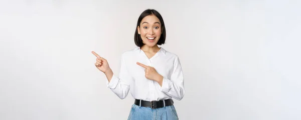 兴奋的年轻亚洲女人的画像，女职员指着打折后的手指，展示销售横幅，站在白色的背景上 — 图库照片