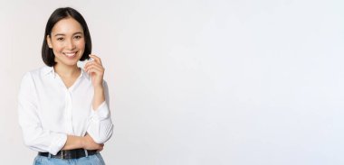 Genç Asyalı kadın, profesyonel girişimci ofis kıyafetleri içinde, gülümsüyor ve kendinden emin görünüyor, beyaz arkaplan