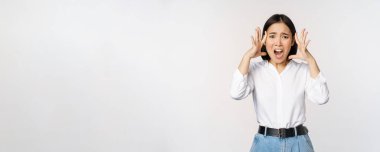 Paniklemiş endişeli Asyalı bir kadın resmi. El ele tutuşmuş, endişeleniyor, hayal kırıklığına uğramış ve beyaz arka plana karşı korkmuş.