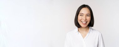 Gülümseyen Asyalı kadın tasviri, smth 'i düşünmek, hayal kurmak, kendini beğenmiş yüzüyle beyaz arka planda durmak.