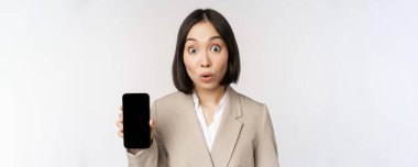 Asyalı kurumsal kadın imajı uygulama arayüzü, cep telefonu ekranı gösteriyor, şaşırmış yüz ifadesi yapıyor, wow, beyaz arka planda duruyor.