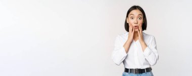 Asyalı kadın modelin görüntüsü şaşırmış, şaşkın şaşkın bakıyor, büyük haberlere tepki veriyor, beyaz arka planda duruyor.