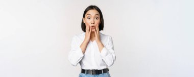 Asyalı kadın modelin görüntüsü şaşırmış, şaşkın şaşkın bakıyor, büyük haberlere tepki veriyor, beyaz arka planda duruyor.