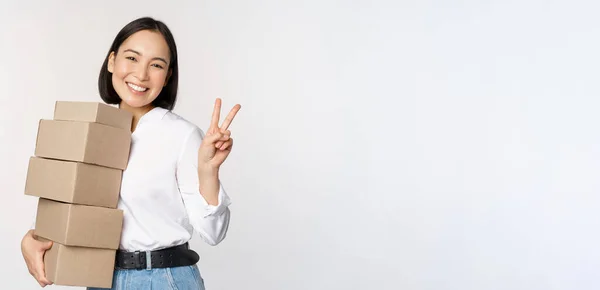 Lächelnde Koreanerin mit Schachteln mit V-Zeichen, Friedensgeste, auf weißem Hintergrund stehend — Stockfoto