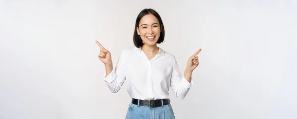 Imagen de hermosa mujer asiática señalando los dedos izquierda y derecha, tomando decisiones, mostrando dos variantes opciones, de pie sobre fondo blanco —  Fotos de Stock
