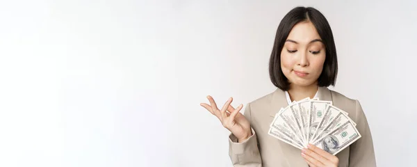 Bild av asiatisk företagskvinna, glad affärskvinna visar pengar, kontanter dollar och tänkande, står i kostym över vit bakgrund — Stockfoto