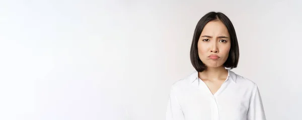 Triste e sombrio jovem asiático mulher sorridente, franzindo a testa chateado, fazendo cara de amuado, fundo branco — Fotografia de Stock