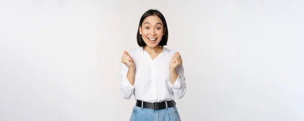 Enthusiastische asiatische Frau jubelt, sagt ja, sieht glücklich aus und feiert den Sieg, Meistertanz, Faust-Pump-Geste, steht über weißem Hintergrund — Stockfoto
