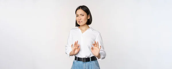 No, gracias. Joven mujer asiática disgustada declinando propuesta, estrechando las manos y paso atrás, mirando con aversión, rechazando oferta, de pie sobre fondo blanco — Foto de Stock