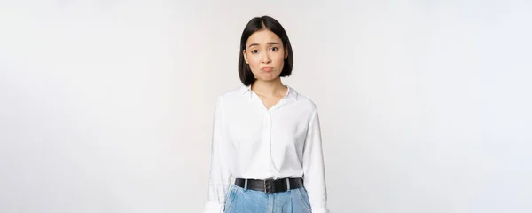 Kép szomorú irodai lány, ázsiai nő duzzogó és homlokráncoló csalódott, álló ideges és zaklatott ellen fehér háttér — Stock Fotó
