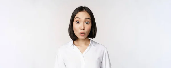 Close-up portret van jonge aziatische vrouw model kijken verbaasd op camera, glimlachende witte tanden, staande tegen witte achtergrond — Stockfoto