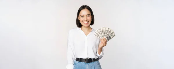 Kredit- och lånebegreppet. Leende ung asiatisk kvinna som innehar kontanter dollar och ser glad ut på kameran, vit bakgrund — Stockfoto