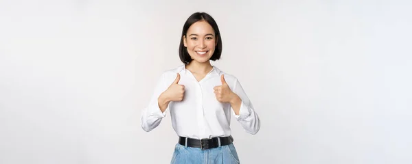 Imagem de bela mulher asiática adulta mostrando polegares para cima, vestindo escritório formal, roupas universitárias, recomendando companhia, de pé sobre fundo branco — Fotografia de Stock