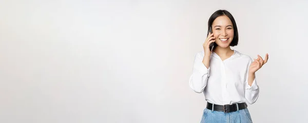 행복 한 아시아인 여성 이 스마트폰으로 고객 과 통화하는 것, 판매원 이 당직으로 전화를 걸는 것, 핸드폰을 들고 몸짓을 하는 것, 백지 배경 위에 서 있는 것 — 스톡 사진