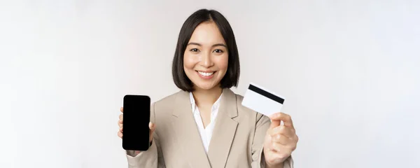 Smiling corporate woman in suit, showing mobile phone screen and app on mobile phone, smartphone screen, standing over white background — Stock Photo, Image