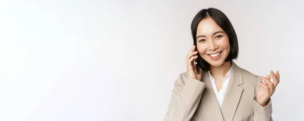 Sorrindo mulher corporativa de terno, falando no telefone celular, tendo uma chamada de negócios no smartphone, de pé sobre fundo branco — Fotografia de Stock