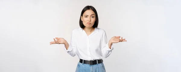 Afbeelding van verwarde aziatische office manager, office lady shrugging schouders en kijken clueless, staande verbaasd tegen witte achtergrond — Stockfoto