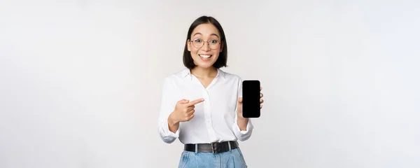 Entusiasta giovane donna asiatica che punta il dito contro lo schermo dello smartphone, mostrando pubblicità sul telefono cellulare, sfondo bianco — Foto Stock