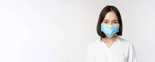 Covid e conceito de saúde. Close up retrato de mulher asiática, office lady in face mask, sorrindo, usando proteção contra coronavírus durante pandemia, fundo branco — Fotografia de Stock