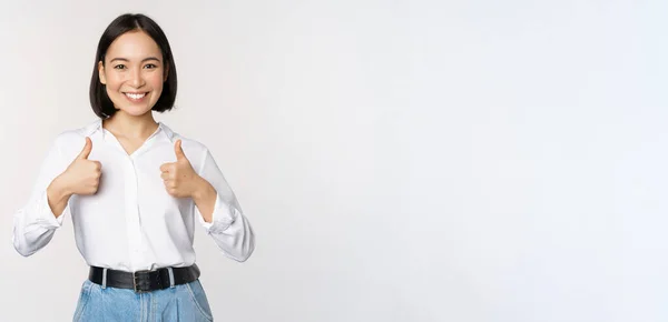 Obrázek krásné dospělé asijské ženy ukazující palce nahoru, na sobě formální kancelář, univerzitní oblečení, doporučující společnost, stojící nad bílým pozadím — Stock fotografie