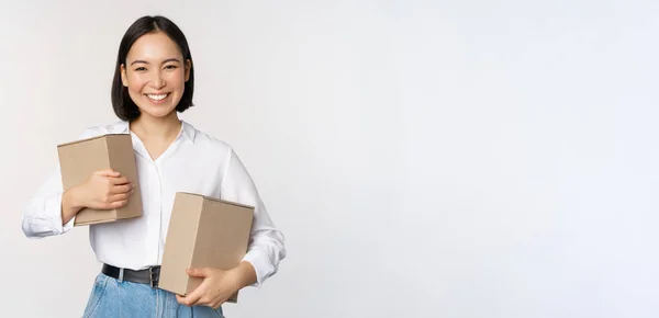 Conceito de compras e entrega. Jovem mulher asiática feliz posando com caixas e sorrindo, de pé sobre fundo branco — Fotografia de Stock