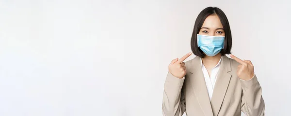 Coronavirus och affärsmän koncept. Asiatisk kvinnlig entreprenör pekar finger åt medicinsk ansiktsmask på arbetsplatsen, står över vit bakgrund — Stockfoto