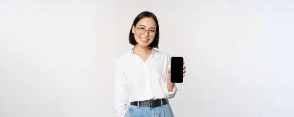 Mujer coreana sonriente mostrando la pantalla del teléfono inteligente, demostrando aplicación móvil, de pie sobre fondo blanco — Foto de Stock